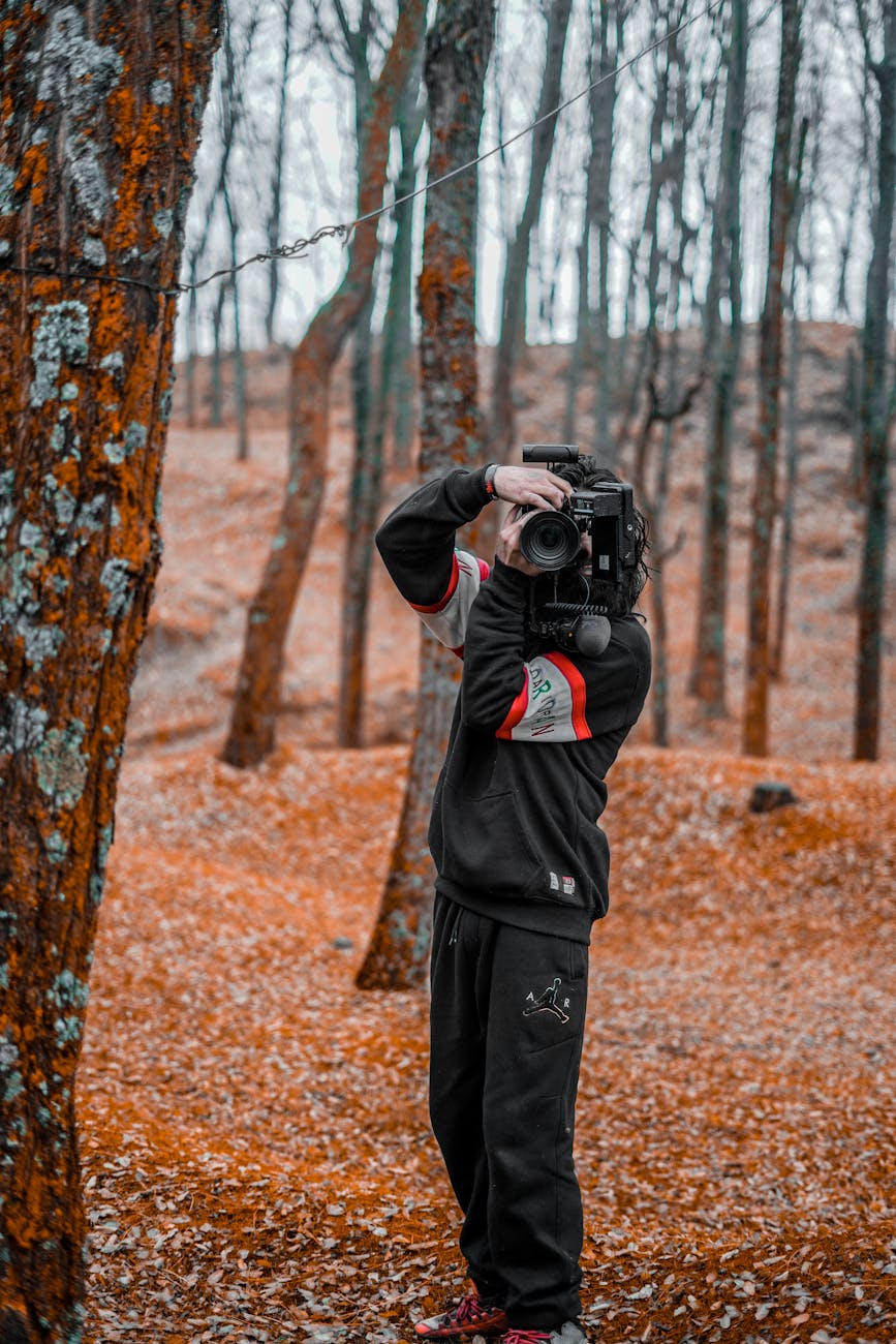 Person using a video camera in a vibrant autumn forest setting.