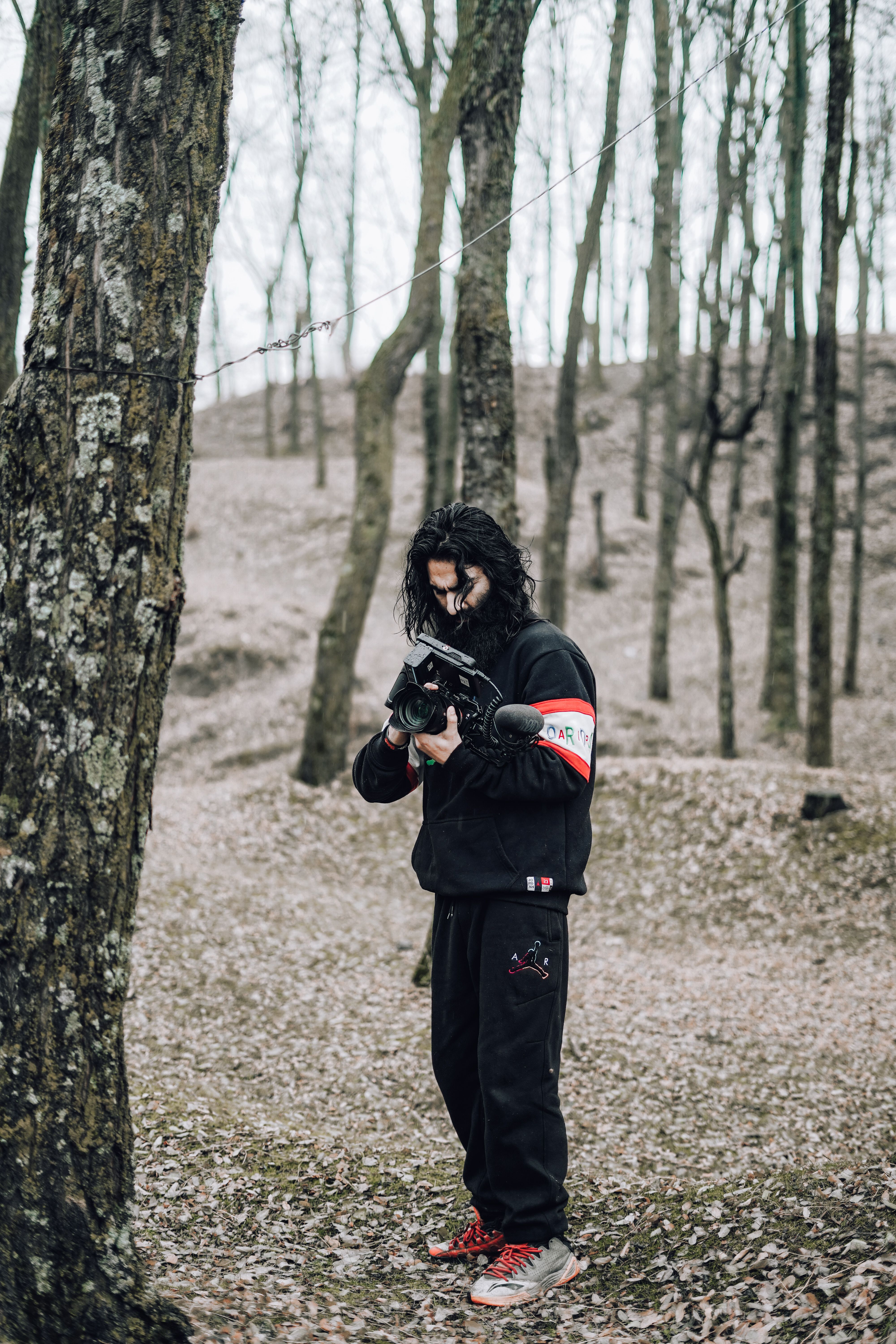 A person in black apparel using a camera in a fall forest.
