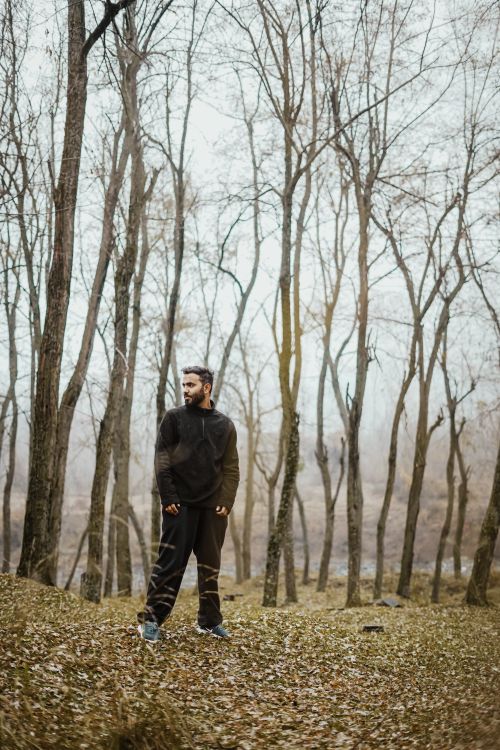 Free A man dressed in dark attire walks through a leafless winter forest, showcasing solitude. Stock Photo
