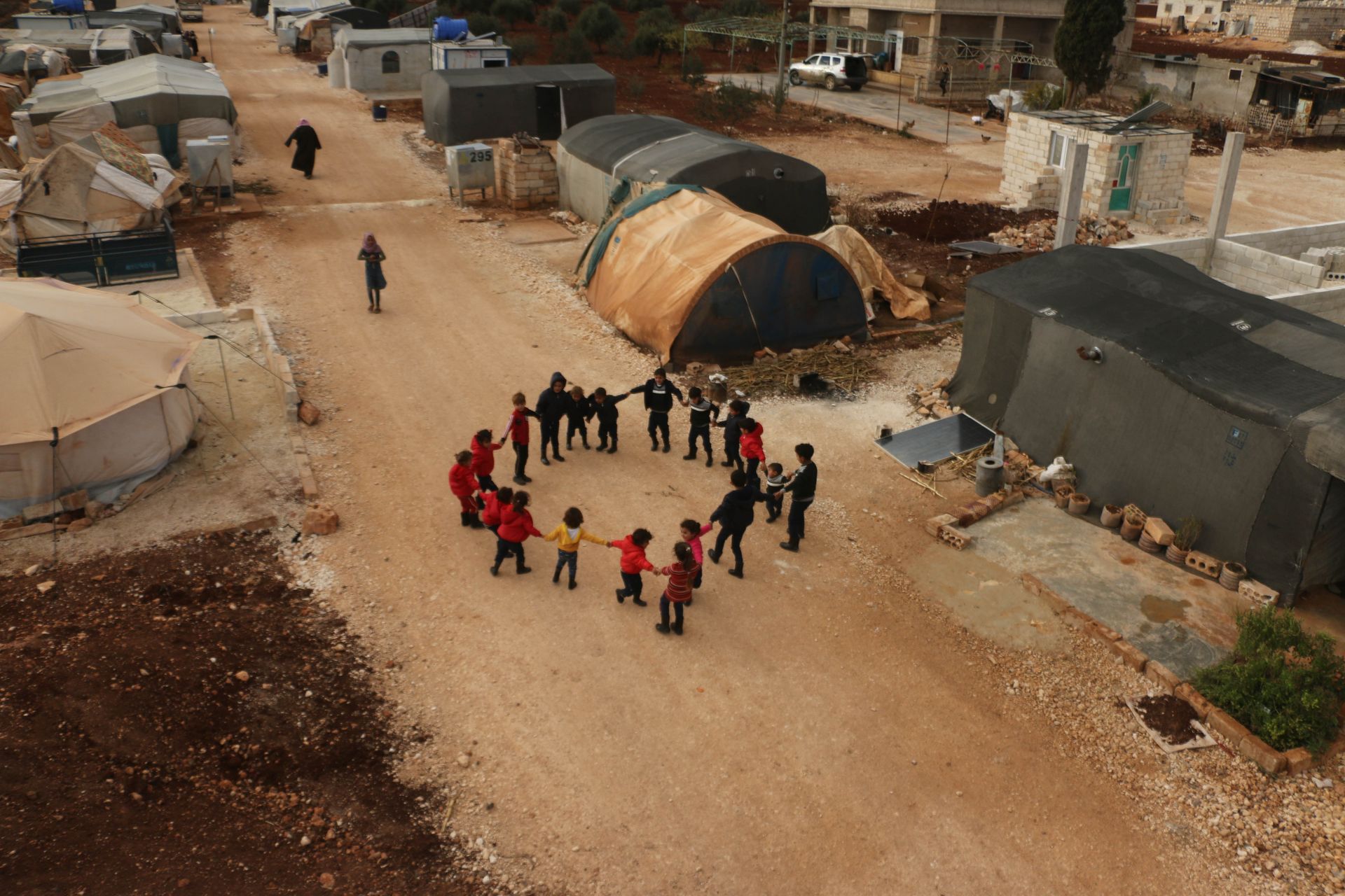 Children play together in a circle at a Syrian refugee camp, capturing a moment of joy and camaraderie.