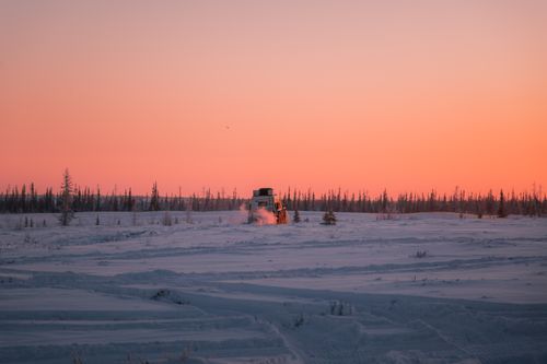 Free A campervan travels across a snowy tundra landscape at sunset, casting a warm hue. Stock Photo