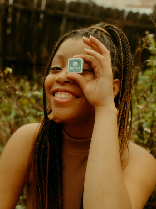 Young Smiling Woman Covering Eye with Square with Pexels logo