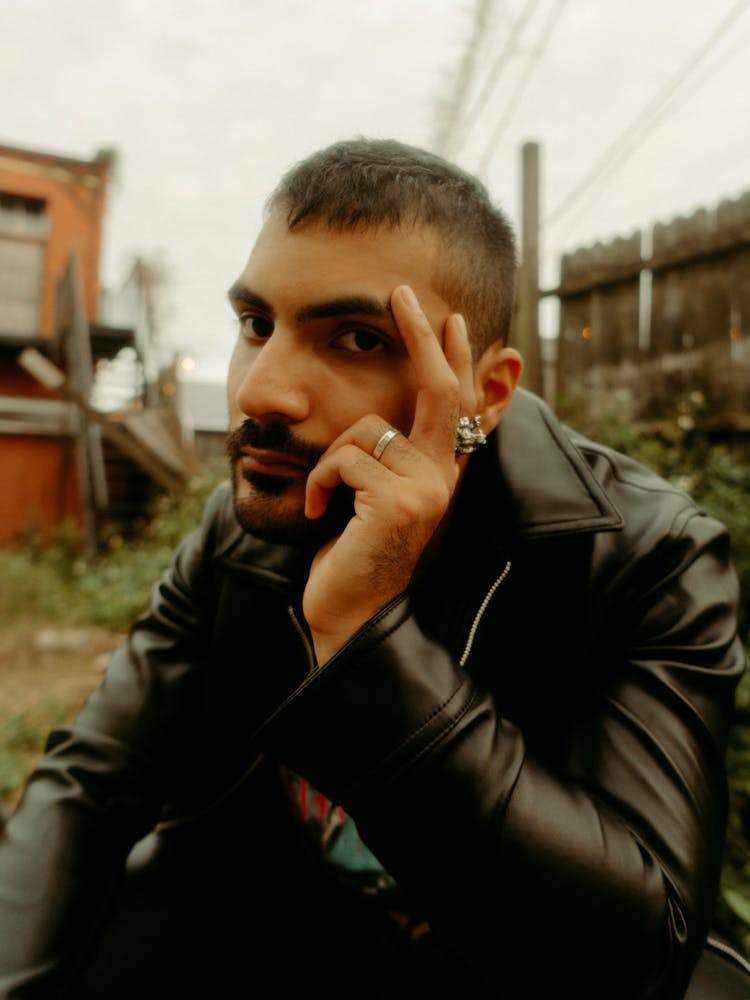 Young Bearded Man Sitting In Messy Backyard And Propping Head With Hand