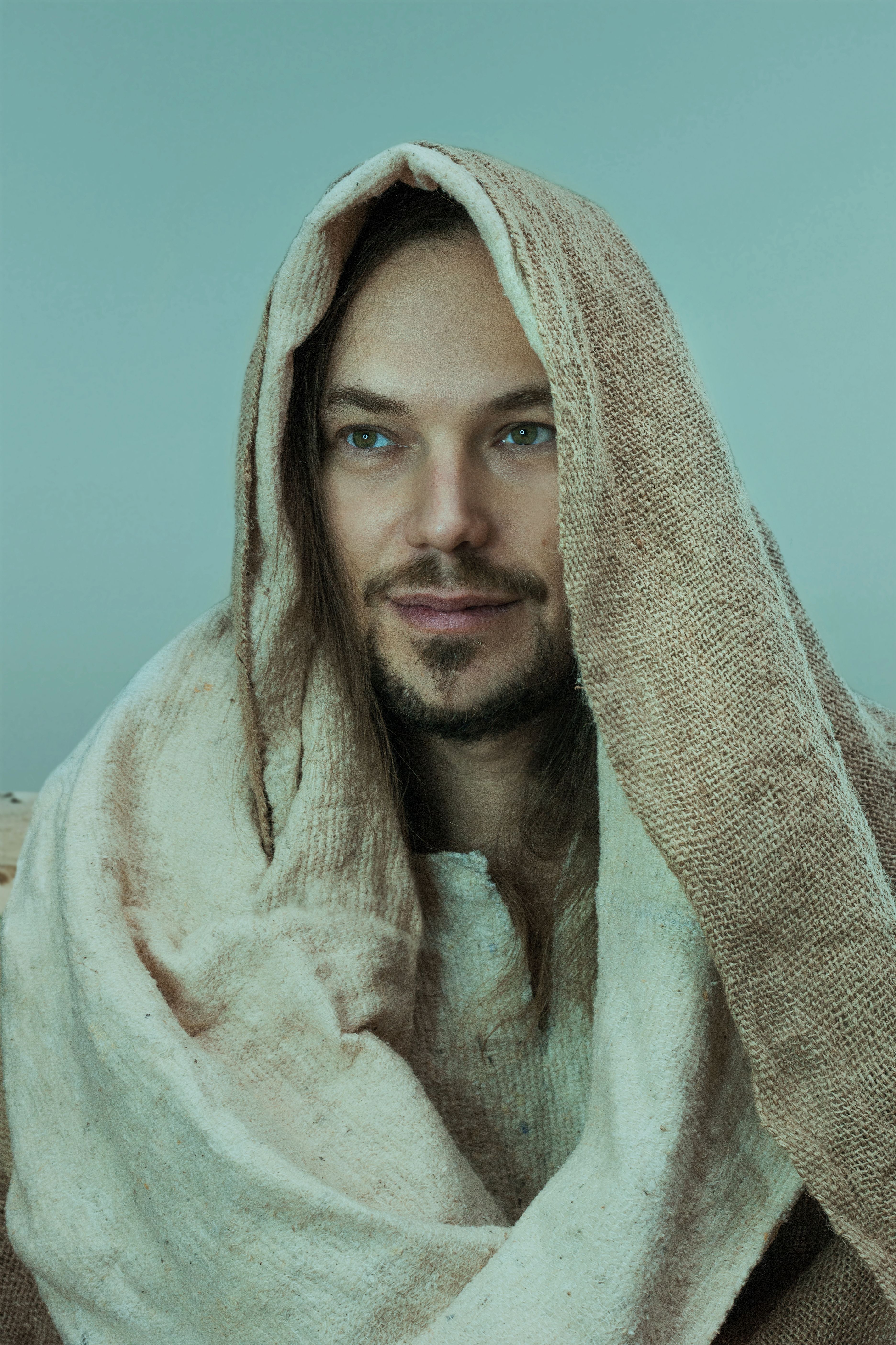 Studio portrait of a man with a beard wearing a beige headscarf, featuring neutral tones.