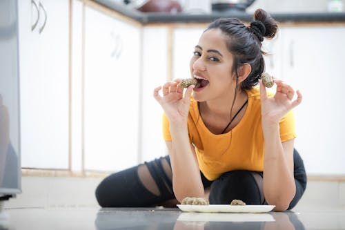 Woman in Orange Shirt Sitting on the Floor While Eating