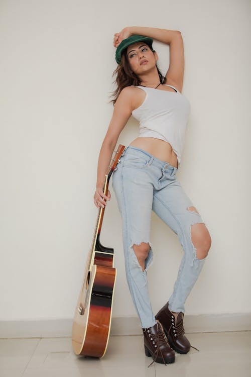 A Woman in White Tank Top and Ripped Jeans Holding a Brown Acoustic Guitar