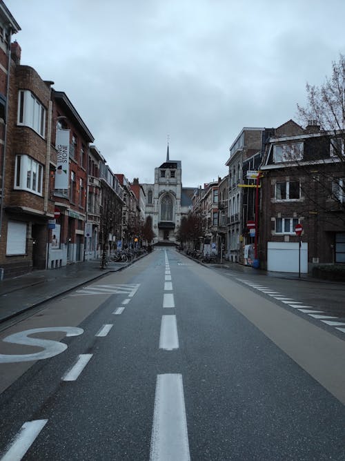 Gray Asphalt Road Between Brown Concrete Buildings Under White Clouds