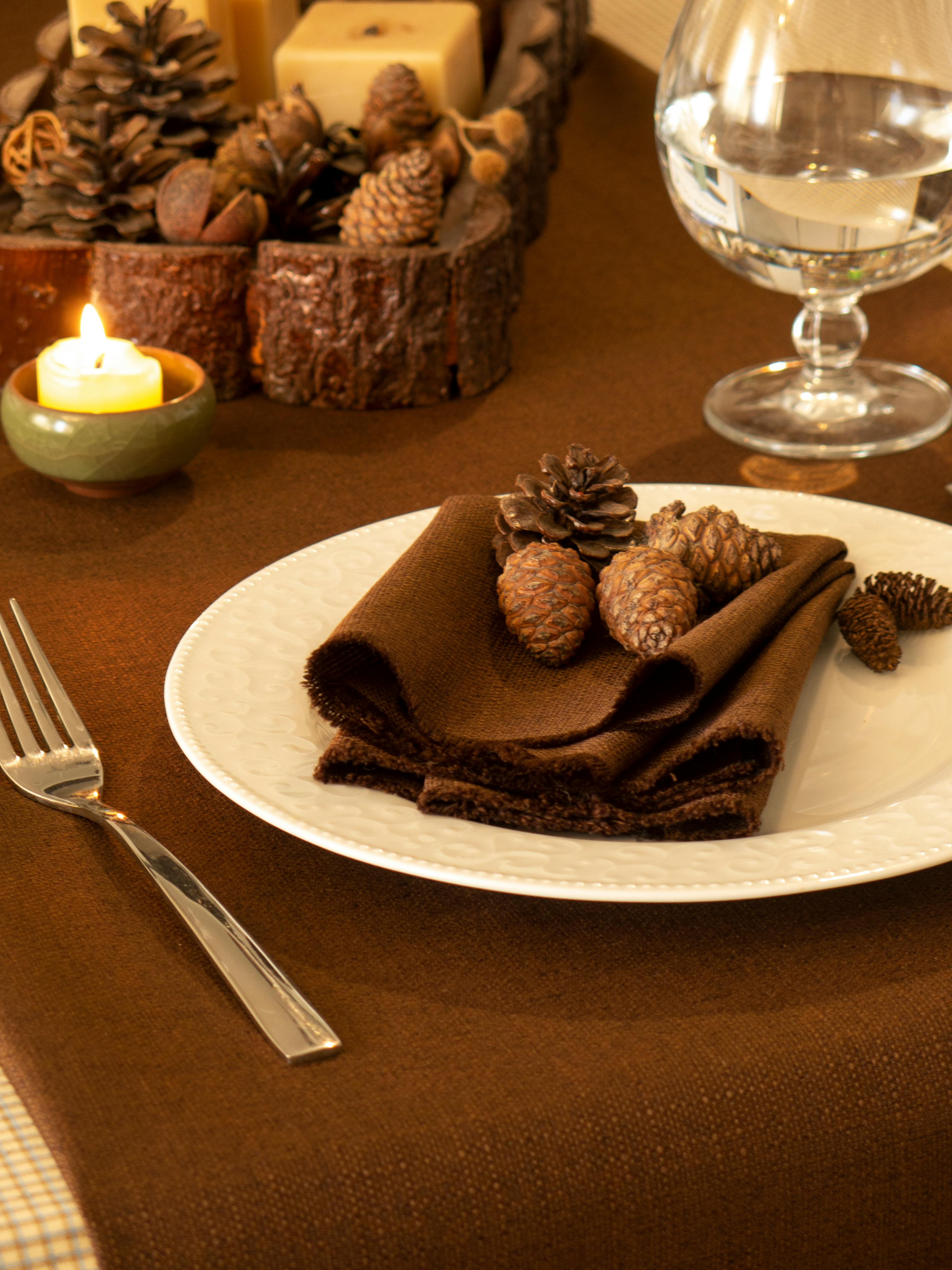 Warm autumn table setting with candles and pinecones for a cozy meal ambiance.