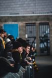 Spectators in hats and warm coats leaning on a rail to watch a game