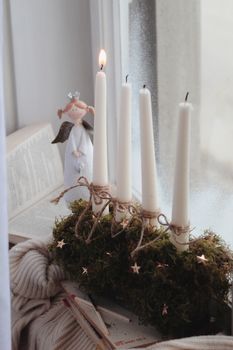 A serene still life featuring candles and an angel figurine by a window, evoking a cozy winter ambiance.