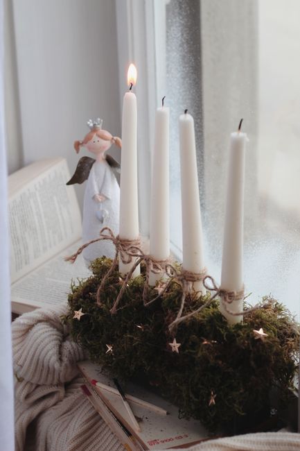 A serene still life featuring candles and an angel figurine by a window, evoking a cozy winter ambiance.