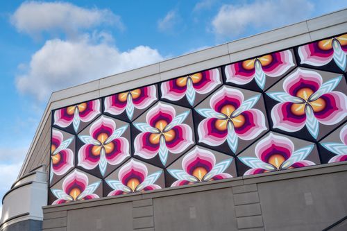 Free A colorful geometric floral mural adorns a modern building façade against a blue sky. Stock Photo