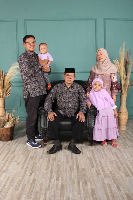 A family poses indoors in traditional clothing and hijabs, smiling together.