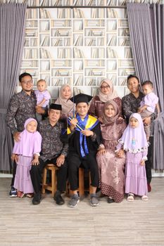 A family gathered in formal attire celebrating a graduation indoors. - Fotografer Sidoarjo