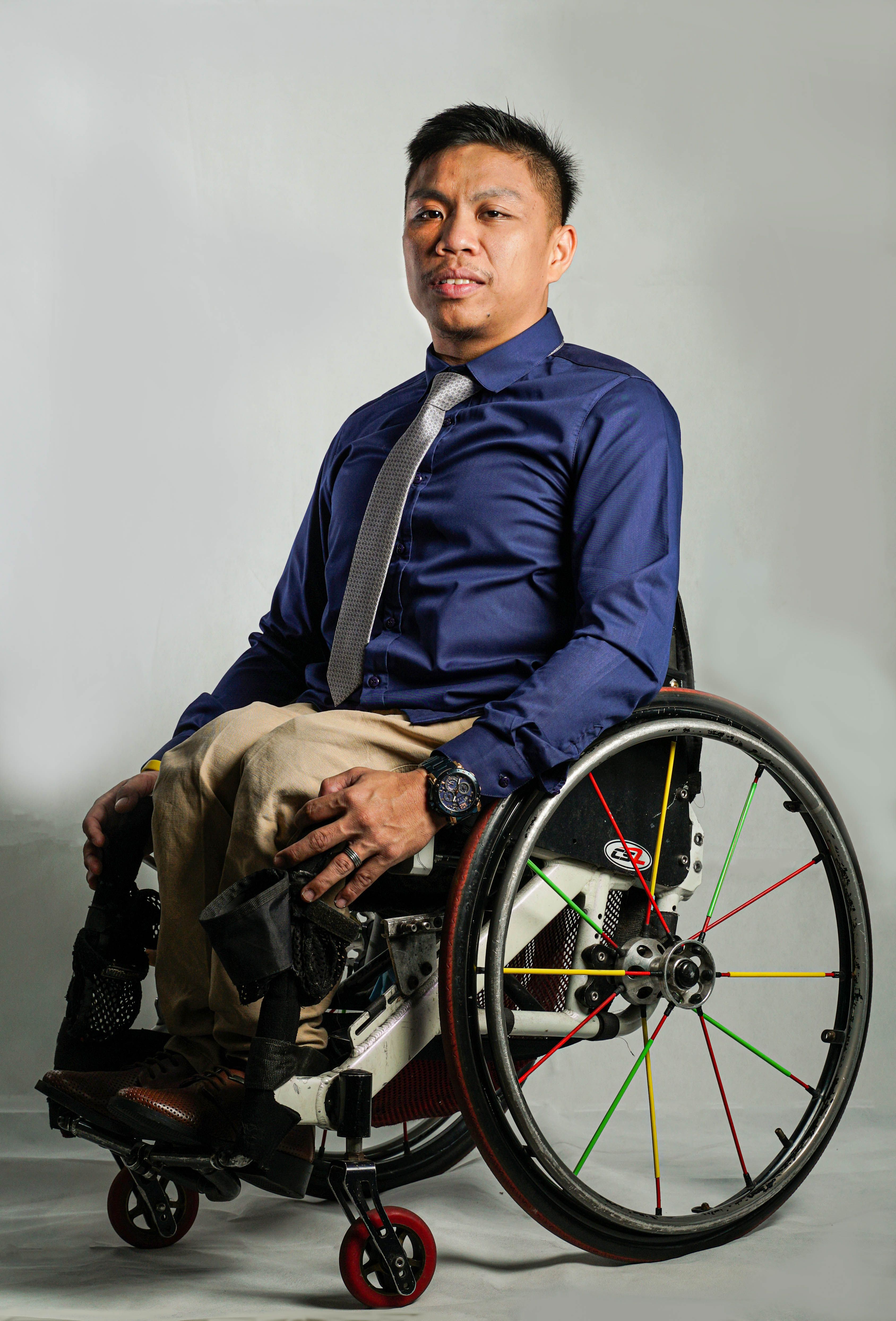Stylish Asian man in a wheelchair wearing a formal shirt and tie in a studio setting.