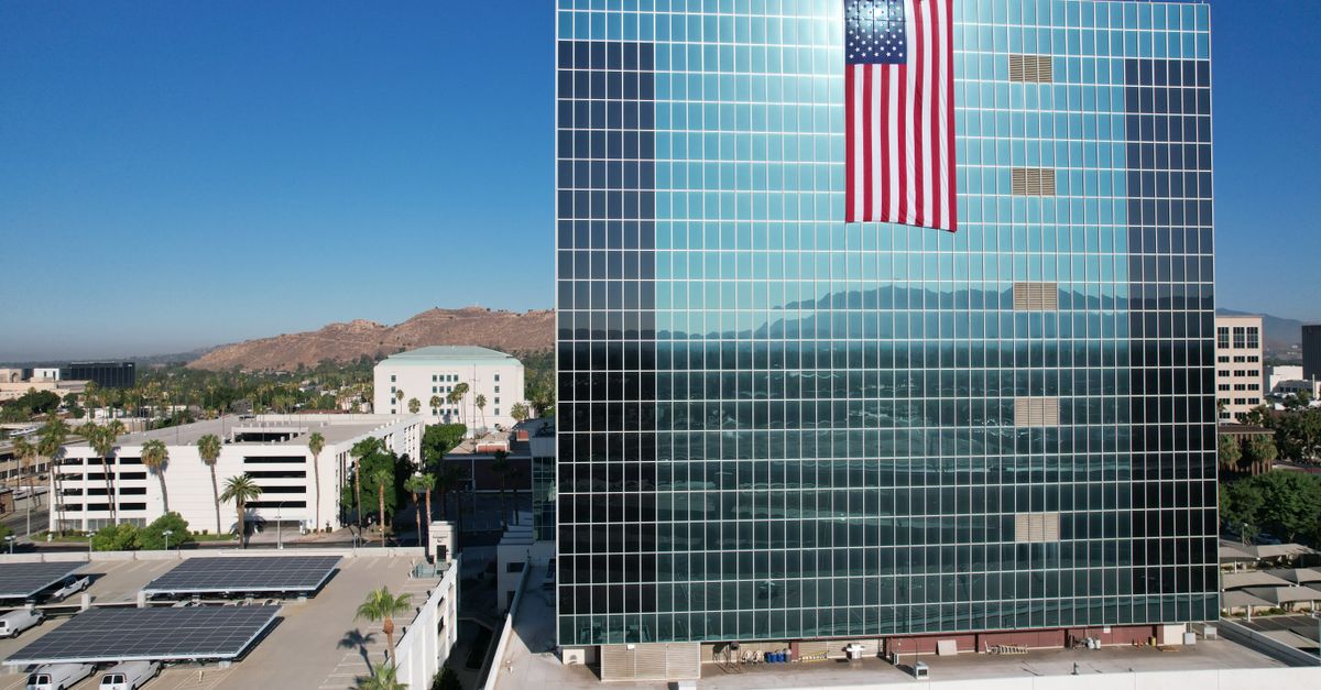 Huge American flag on glass facade building in Riverside, CA, under clear blue sky.