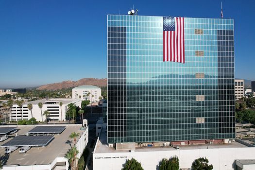 Huge American flag on glass facade building in Riverside, CA, under clear blue sky.