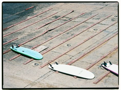 Surfboards laid out on concrete, drying under sunlight, Morocco harbor scene.