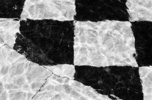 Artistic black and white checkered tiles submerged underwater creating a unique visual pattern.