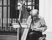 一张黑白图像中，一位年长音乐家在街头演奏竖琴