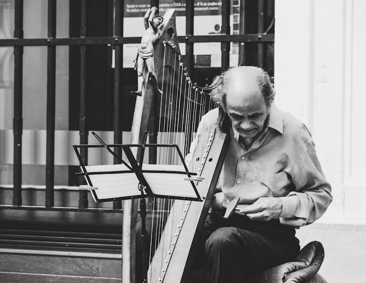 Greyscale Photo Of Man Holding Harp