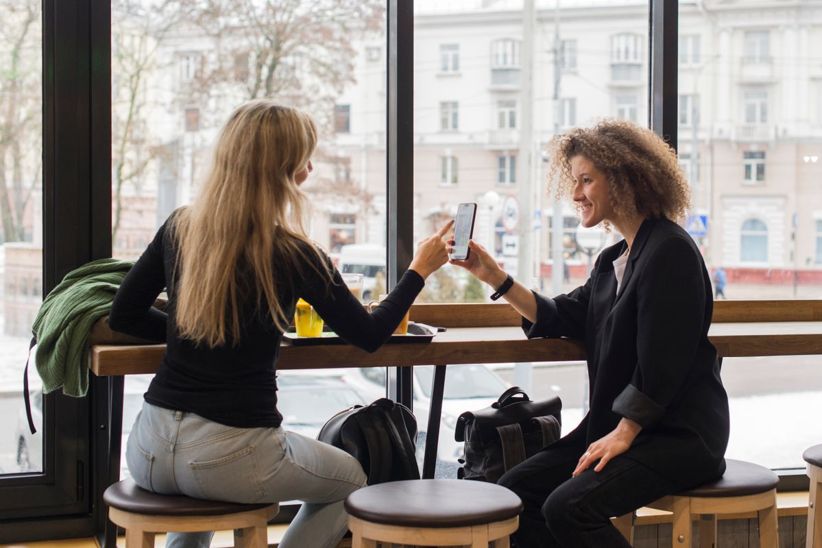 Two women at a café sharing content on a smartphone, enjoying a social moment.