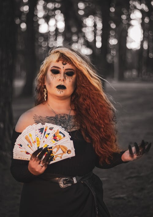 Woman in Black Dress with Dark Makeup and Black Fingers Holding Fan of Cards in the Forest