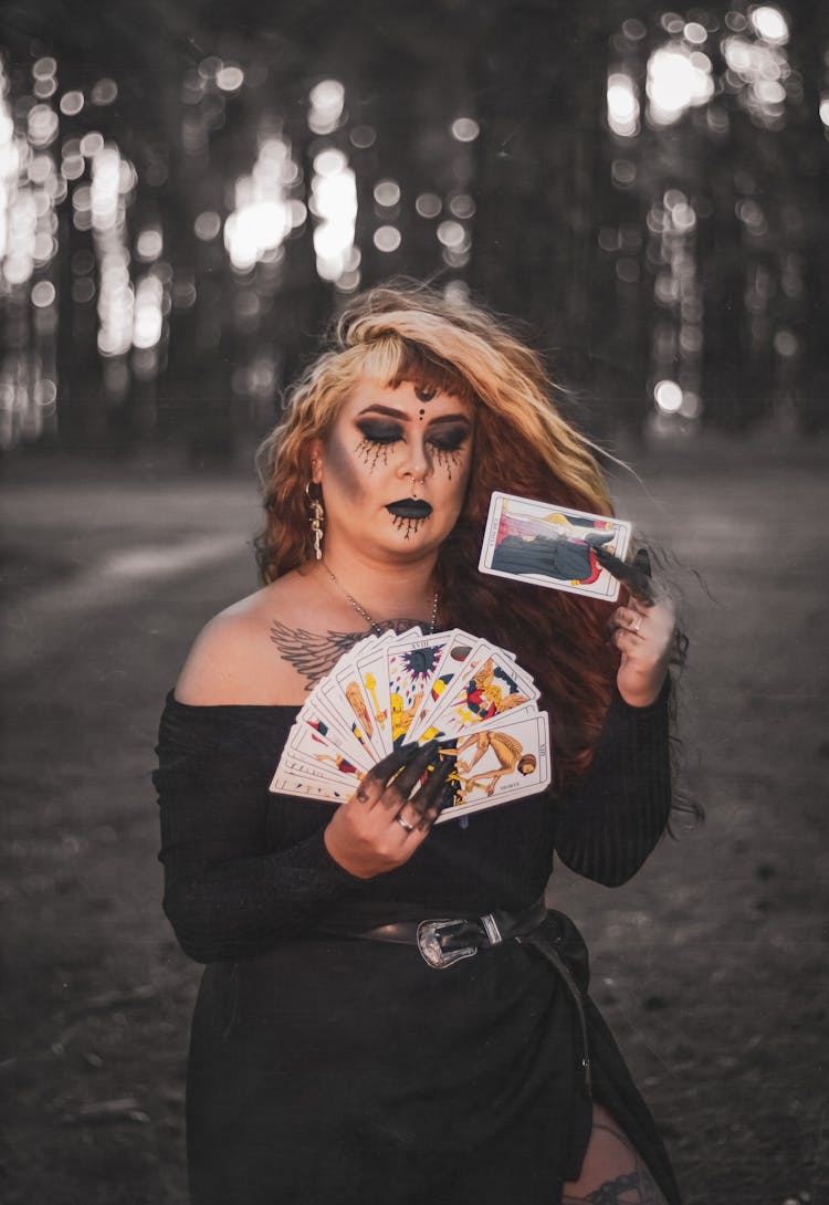 Woman In Black Off Shoulder Long Sleeve Dress Holding Fan Of Tarot Cards In The Forest