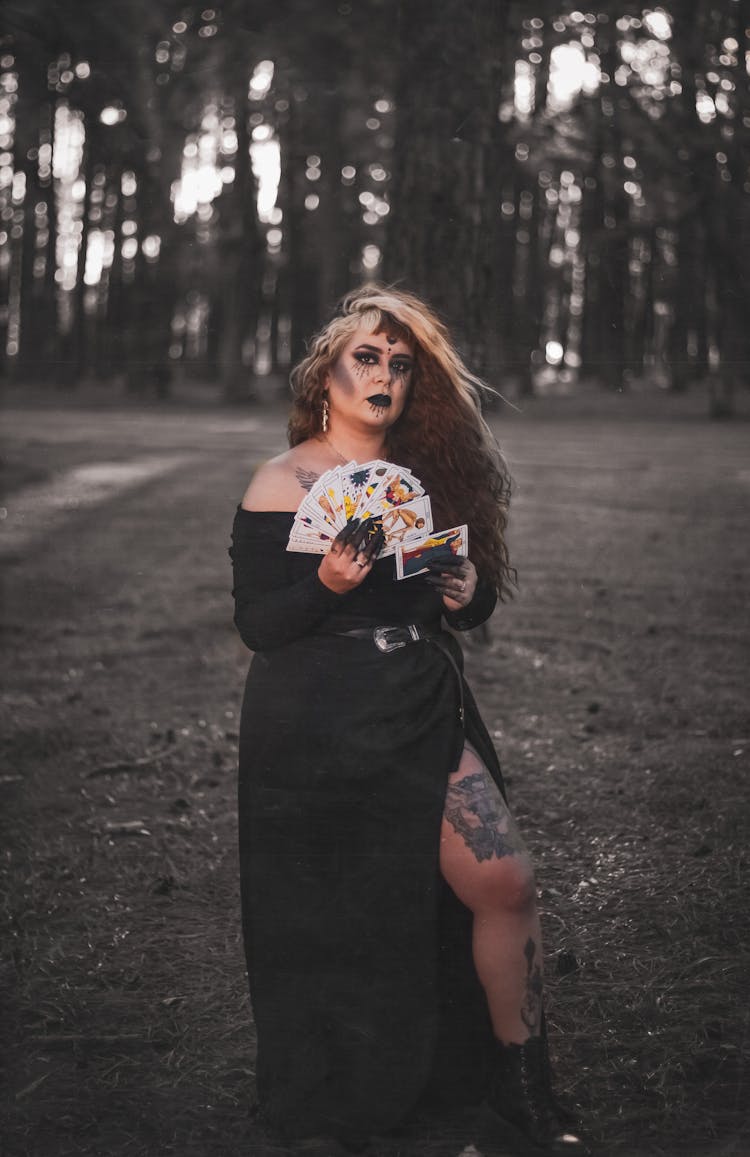 Woman With Long Hair And Tattoos Holding A Deck Of Cards In A Forest