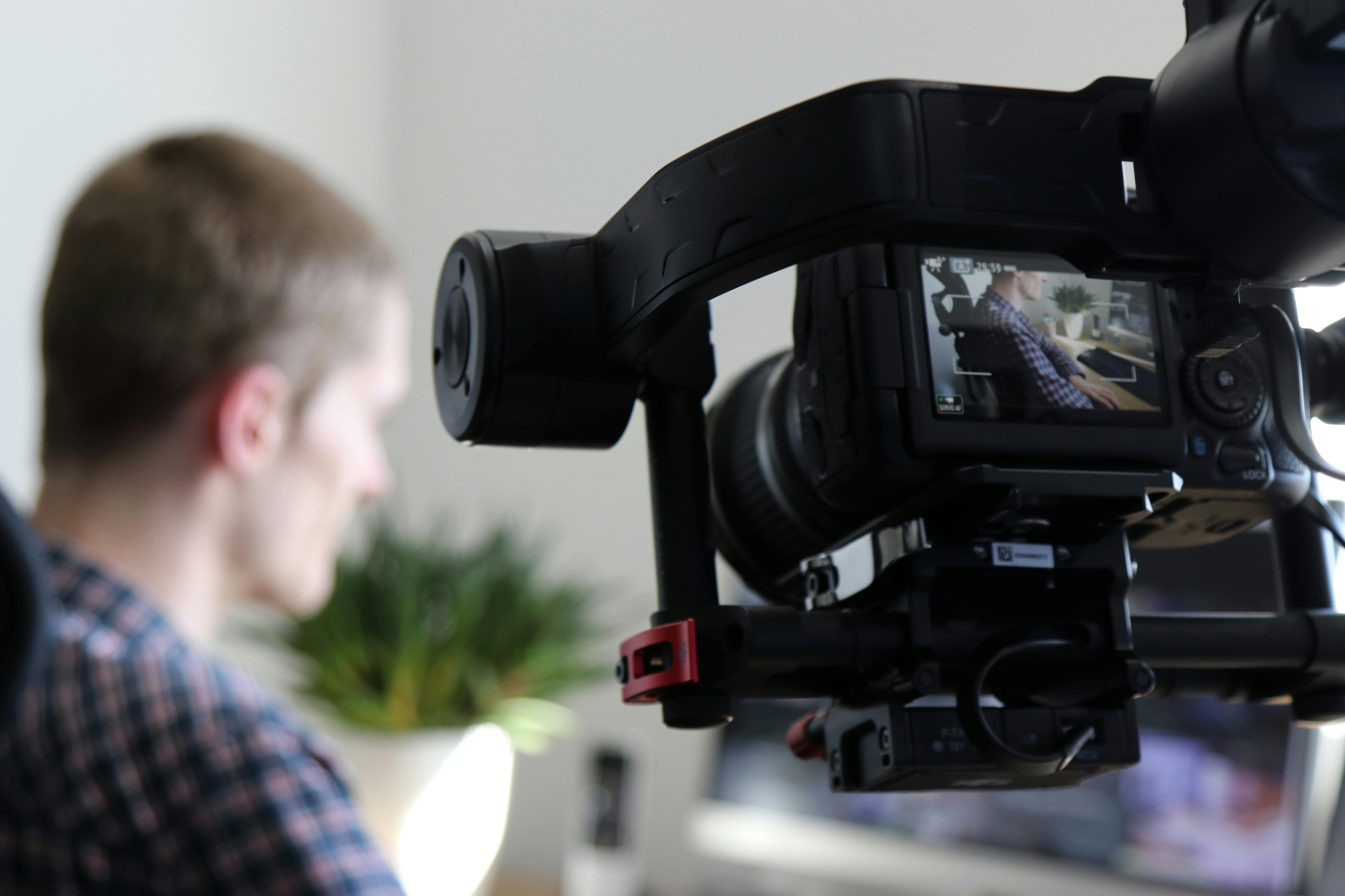 black video camera turn on next to man wears black and gray shirt