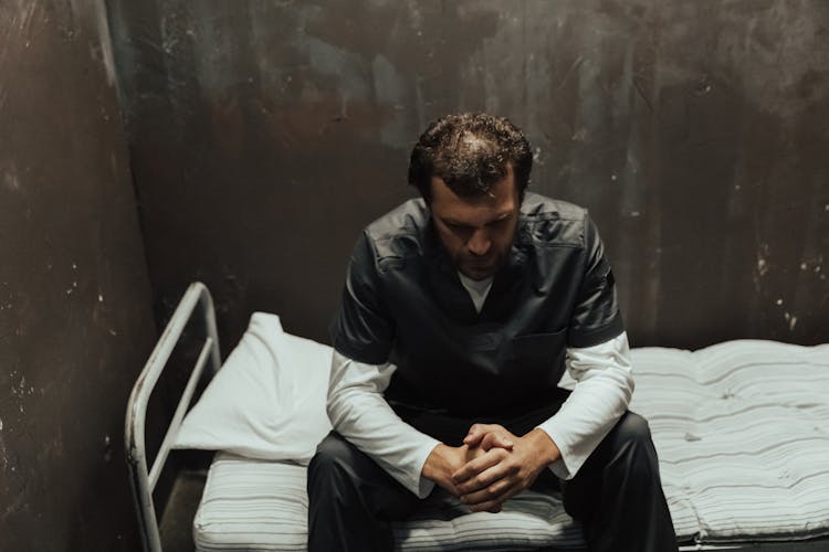 Man Sitting On The Prison Cell Bed