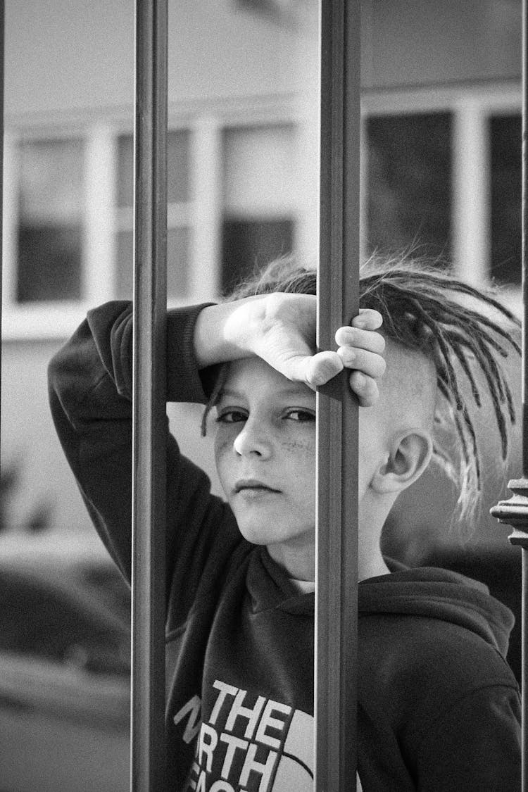 Grayscale Photo Of A Boy With Dreadlocks Holding On To A Steel Bar