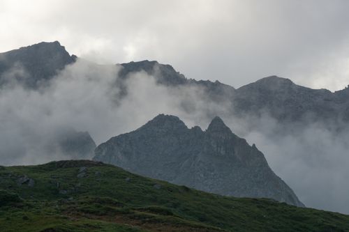 Free Stunning view of misty mountain peaks enveloped in fog with lush green foreground, creating a serene atmosphere. Stock Photo