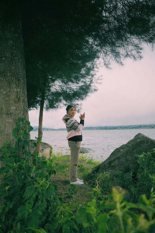 Woman in Hijab and Beige Pants Standing Under the Tree Beside Water