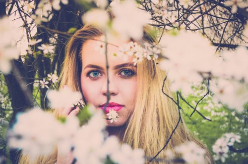 Free Blonde woman with blue eyes surrounded by white flowers in a park setting. Stock Photo
