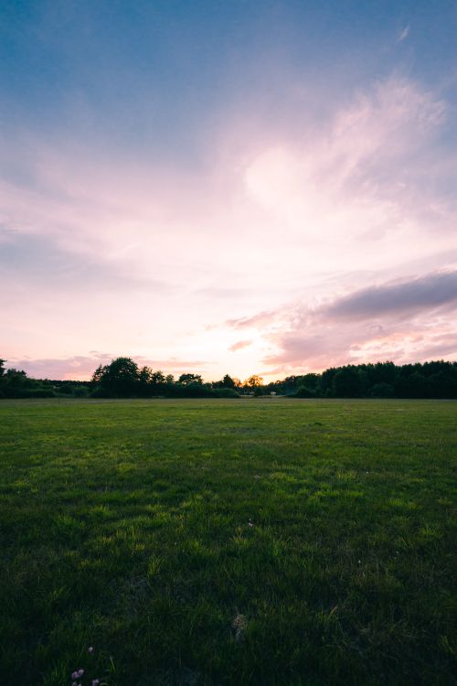 Free A serene countryside field at sunset with a vibrant sky, perfect for landscape photography. Stock Photo