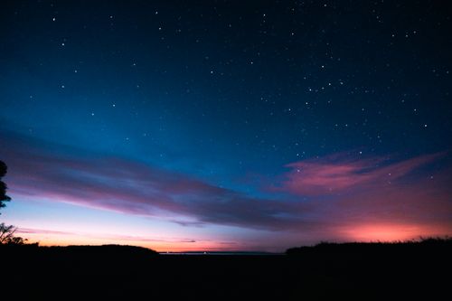 Free A breathtaking view of the night sky with stars and a vibrant cloudscape. Perfect for nature and travel themes. Stock Photo