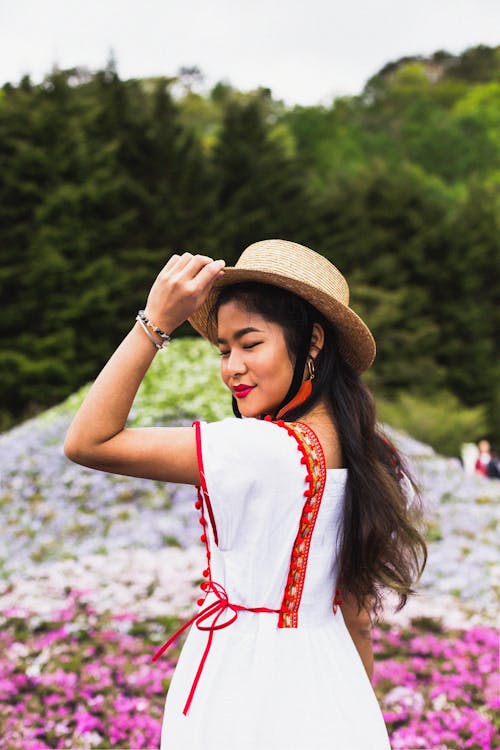 A Woman in Dress Wearing Sun Hat while Standing on a Flower Field