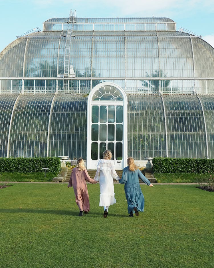 Women Wearing Long Dresses Walking Towards Greenhouse Holding Hands