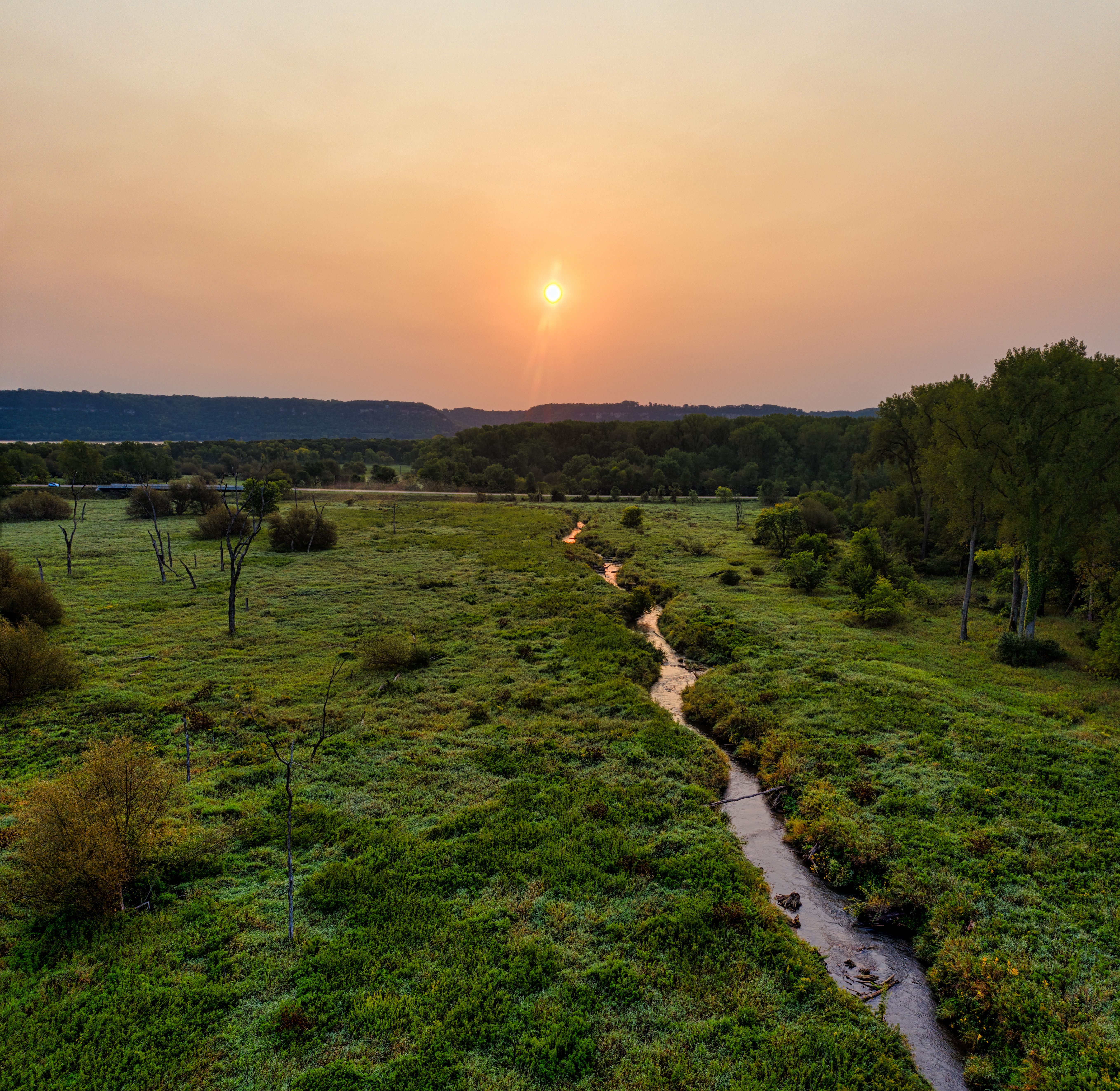 A peaceful sunset over a lush, green landscape with a winding stream, captured in Minnesota.