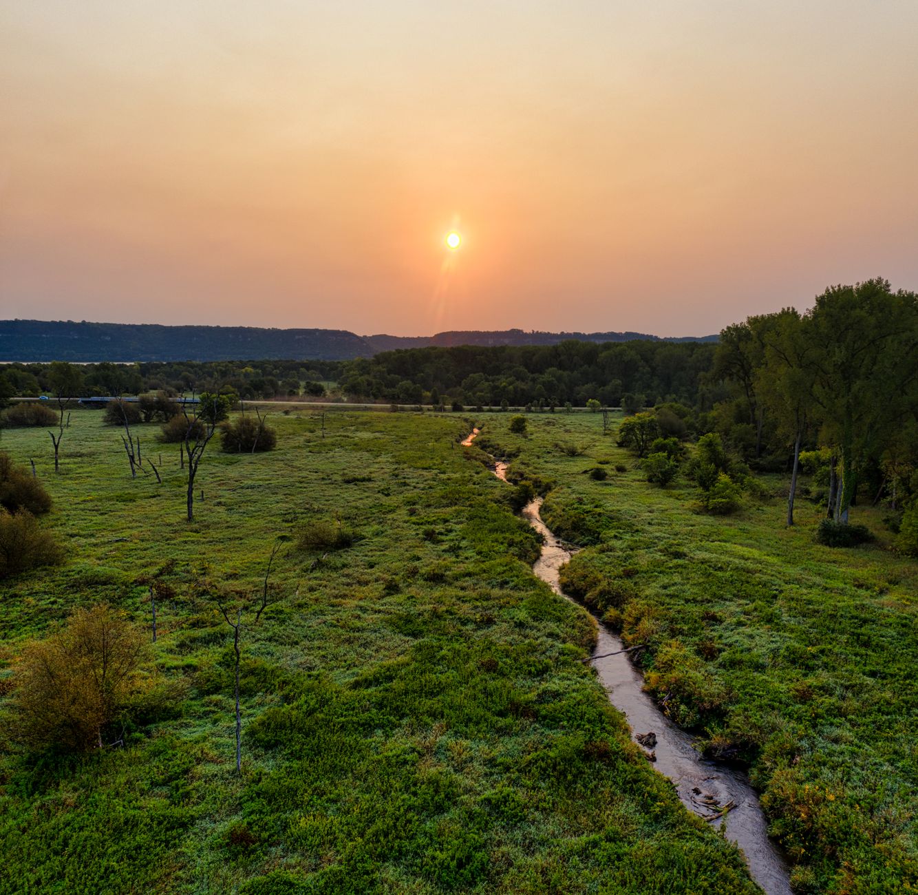A peaceful sunset over a lush, green landscape with a winding stream, captured in Minnesota.