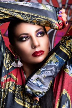 Striking portrait of a woman with vibrant makeup and elegant attire, posing thoughtfully.