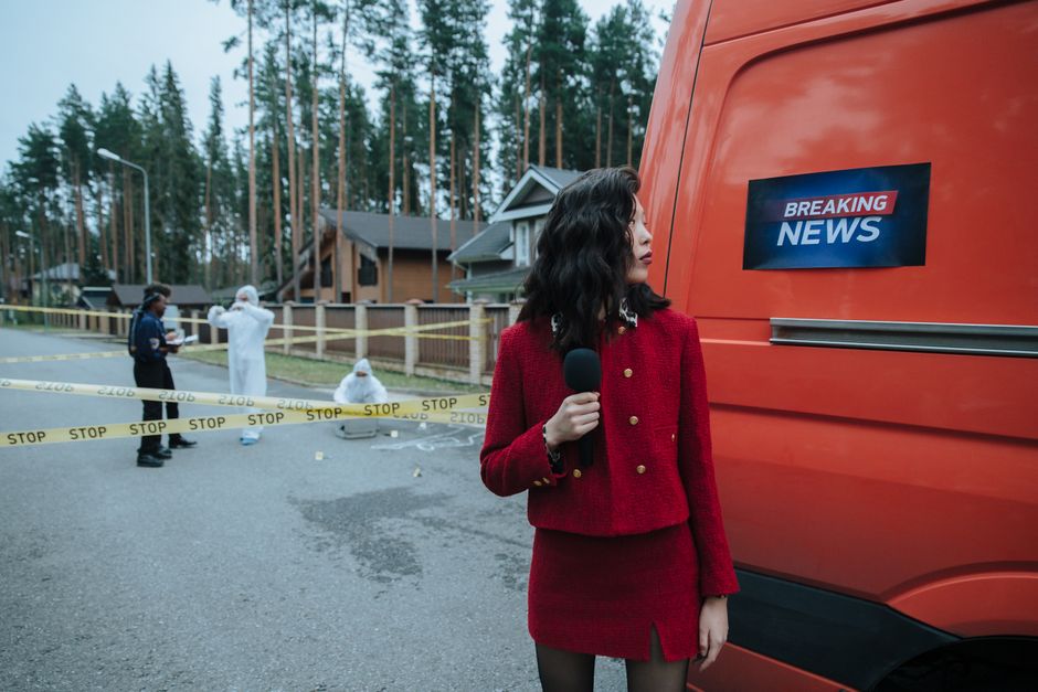 A reporter in red documents a crime scene with investigators in protective suits.
