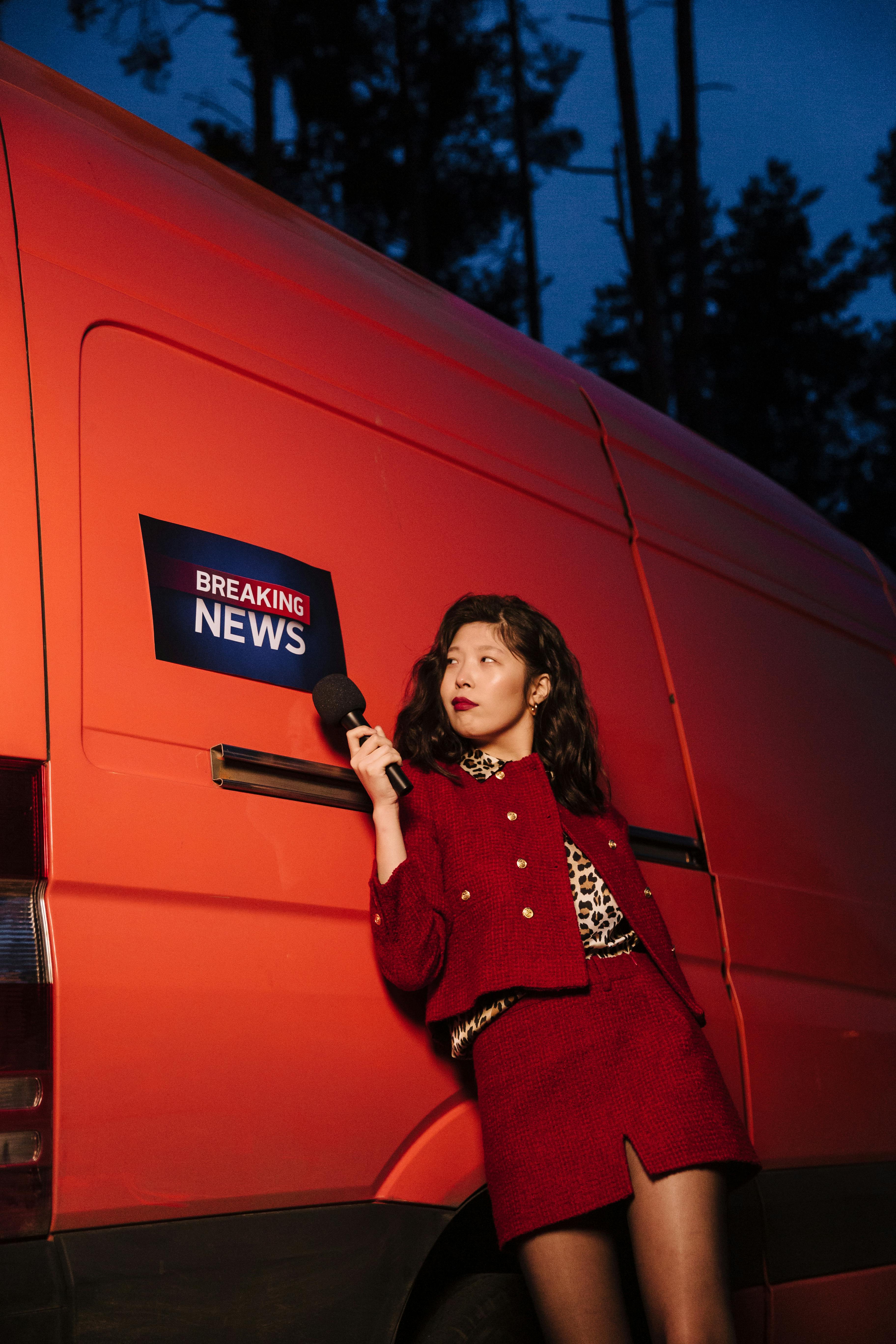 a woman leaning on a van while holding a microphone