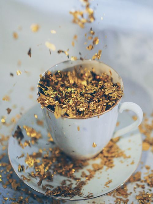 Free A white cup filled with shimmering gold glitter, captured in a burst of sparkles. Stock Photo