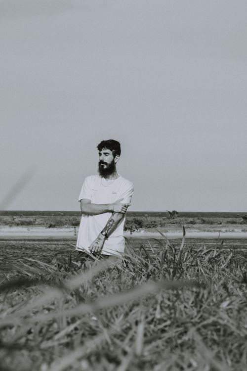 Free Bearded man standing in a grassy field in Itacaré, Brazil, captured in monochrome. Stock Photo
