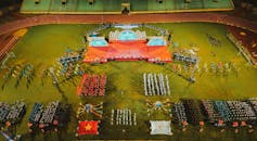 航拍镜头充满活力地捕捉了体育场内，有组织的团体和旗帜参与的体育赛事