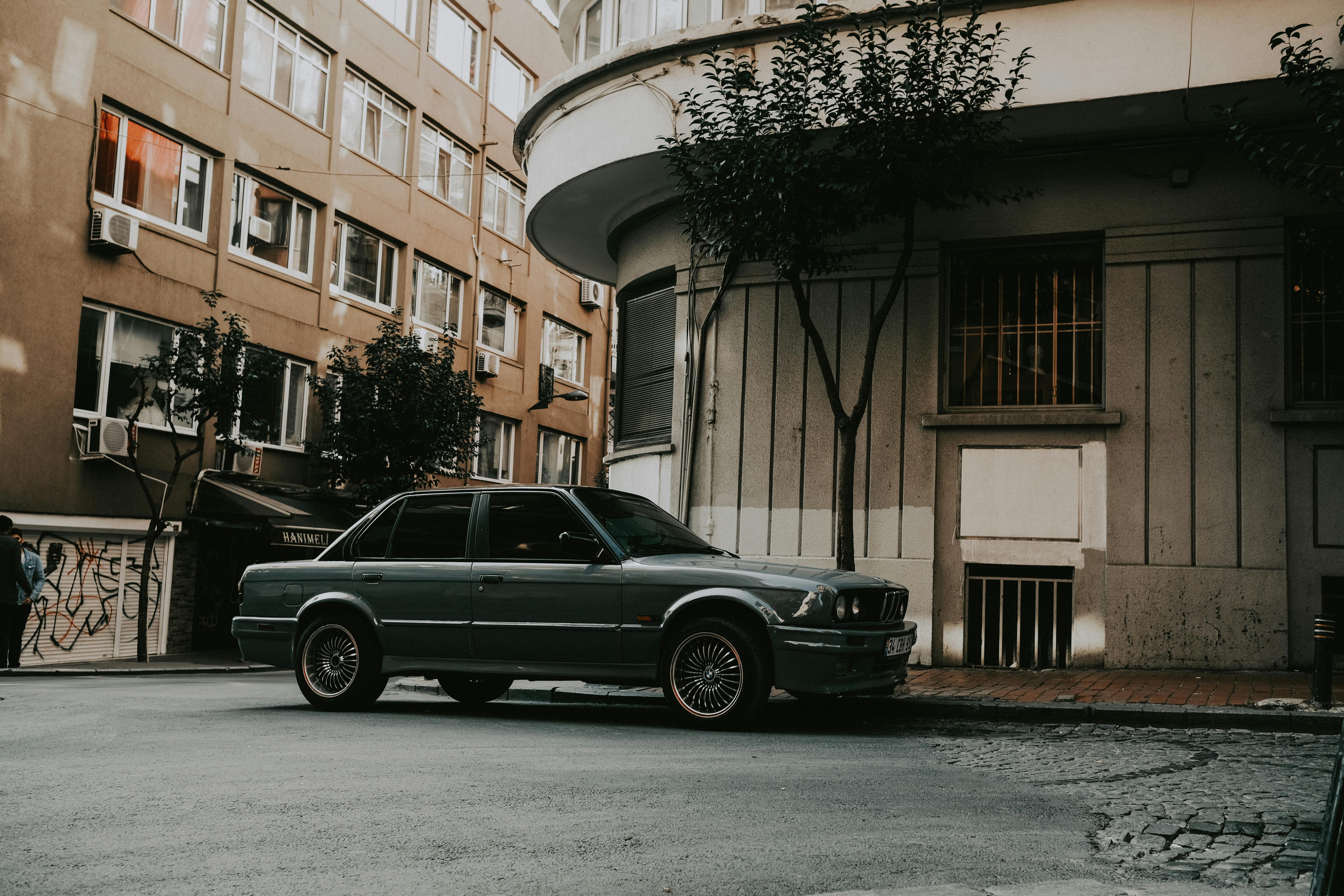 Free A classic car is parked on a city street, surrounded by urban architecture and trees. Stock Photo