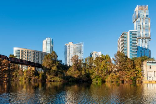 Free City skyline with skyscrapers, bridge, and river surrounded by autumn trees. Stock Photo