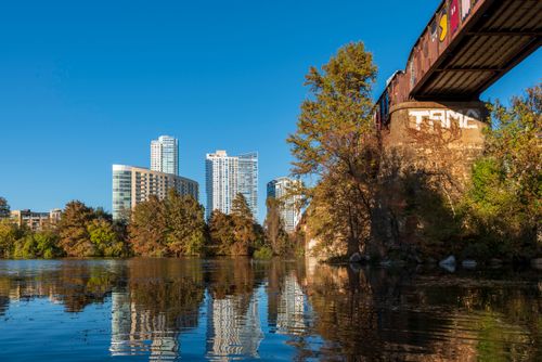 Free A vibrant city skyline with a bridge reflected in a calm river under a clear blue sky. Stock Photo